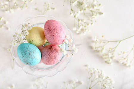 Glass bowl with painted Easter eggs and flowers on light backgroundの写真素材