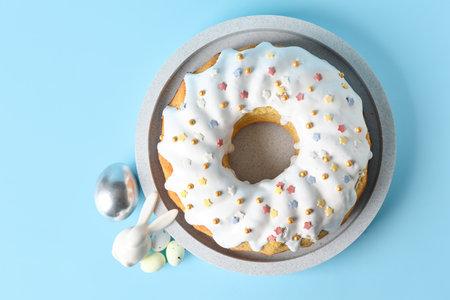 Plate with tasty Easter cake, eggs and decor on blue background