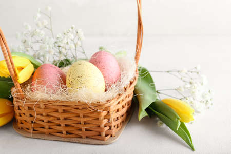 Basket with beautiful Easter eggs and spring flowers on light background, closeup
