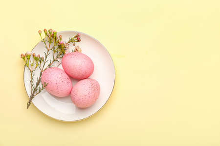 Plate with beautiful Easter eggs and flowers on color backgroundの写真素材