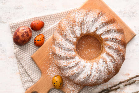 Wooden board with tasty Easter cake and eggs on light background