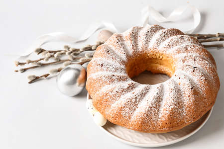 Plate with tasty Easter cake, willow branches and eggs on light backgroundの写真素材
