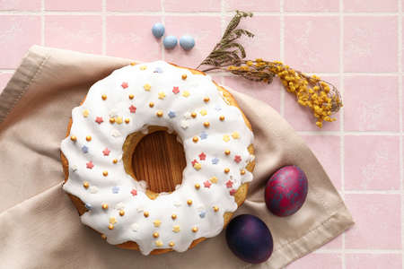 Wooden board with tasty Easter cake and eggs on tile background