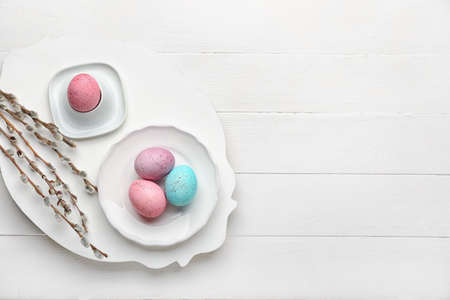 Plate with beautiful Easter eggs and pussy willow branches on light wooden backgroundの写真素材