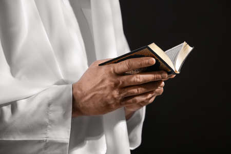 Muslim man with Koran on dark background, closeup