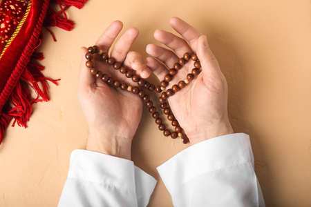 Hands of praying Muslim man with tasbih on color backgroundの写真素材