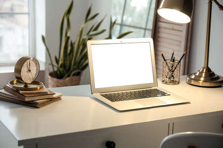 Modern laptop and glowing lamp on table in roomの写真素材