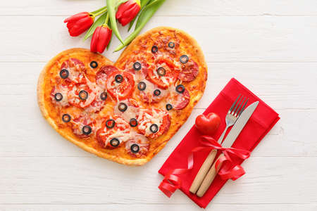 Tasty heart-shaped pizza and tulip flowers on white wooden background. Valentine's Day celebrationの写真素材