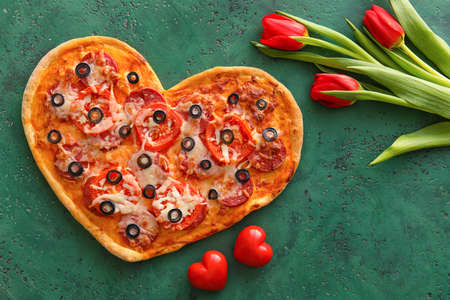Tasty heart-shaped pizza and tulip flowers on green background. Valentine's Day celebrationの写真素材