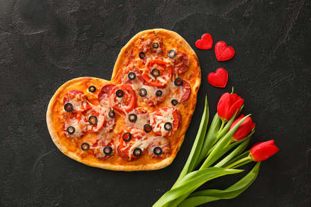 Tasty heart-shaped pizza and tulip flowers on black background. Valentine's Day celebrationの写真素材