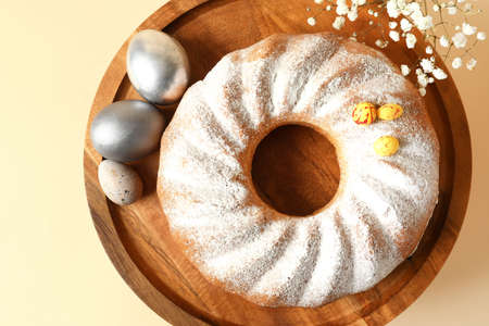 Dessert stand with tasty Easter cake, gypsophila flowers and eggs on beige background