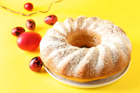 Plate with tasty Easter cake and eggs on yellow background