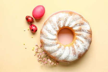 Plate with tasty Easter cake, eggs and gypsophila flowers on beige background