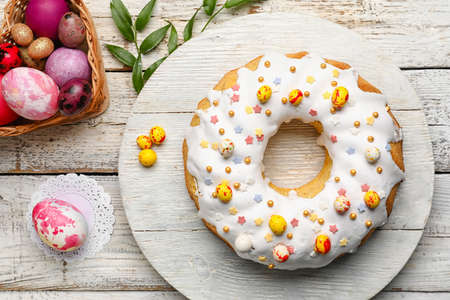 Board with tasty Easter cake and eggs on white wooden background