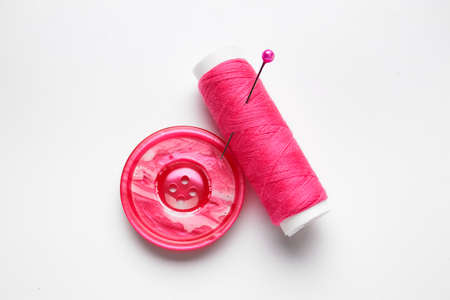 Thread spool with button and needle on white background