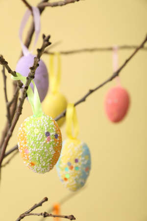 Composition with different Easter eggs hanging on tree branches against color background, closeup