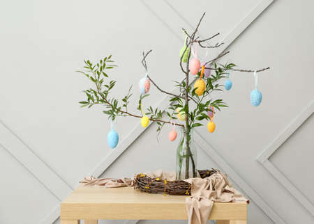 Composition with green tree branches and Easter eggs on table near gray wall