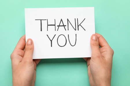 Female hands holding sheet of paper with text THANK YOU on turquoise backgroundの写真素材