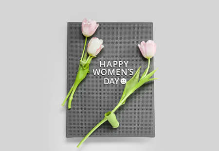 Board with text HAPPY WOMEN'S DAY and tulips on gray background
