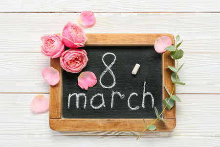 Chalkboard with text 8 MARCH and flowers on white wooden background