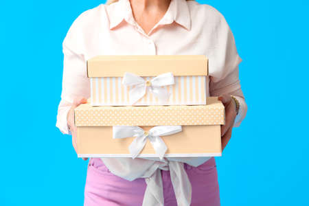 Mature woman holding stack of gift boxes on blue background, closeup. International Women's Day celebrationの写真素材