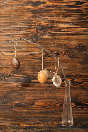 Vase with tree branch and Easter eggs on wooden background