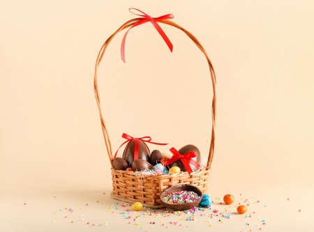 Basket with chocolate Easter eggs, candies and sprinkles on beige background