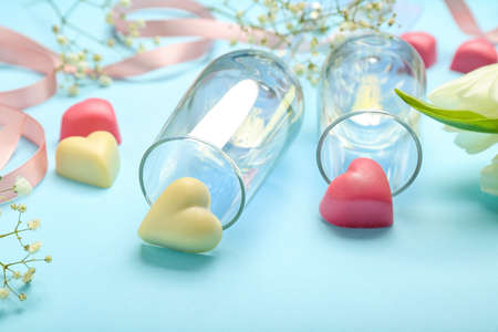 Tasty heart-shaped candies with glasses and flowers for Valentine's Day celebration on blue...