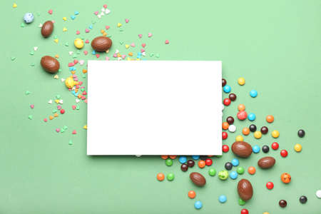 Composition with sheet of paper, chocolate Easter eggs and candies on green background