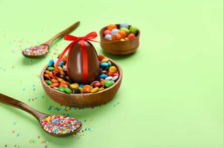 Chocolate Easter egg, candies and sprinkles on green background, closeup