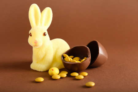 Chocolate Easter egg with candies and bunny on brown background