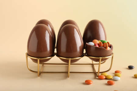 Holder with chocolate Easter eggs and candies on beige backgroundの写真素材