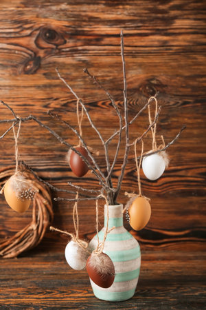 Vase with tree branch and different Easter eggs on wooden background