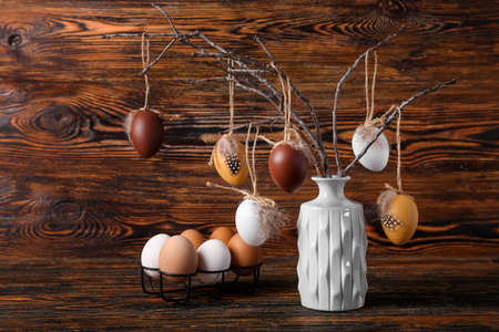 Vase with tree branches and holder with Easter eggs on wooden background