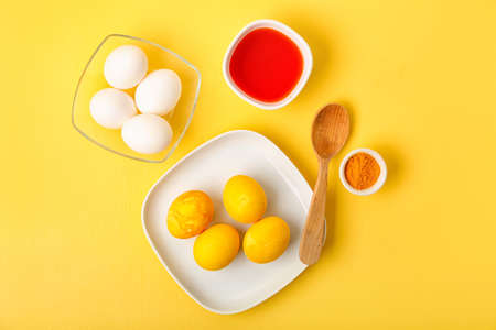 Easter eggs, turmeric powder and bowl with homemade natural dye on color background