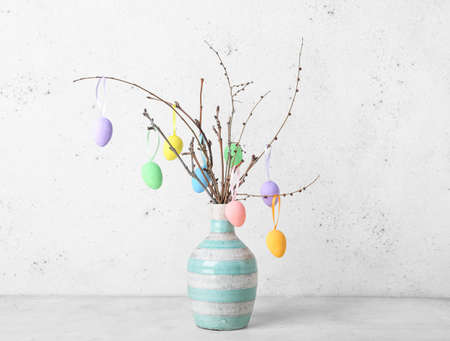 Vase with tree branches and different Easter eggs on light background