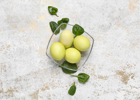 Bowl with beautiful Easter eggs and spinach leaves on light background