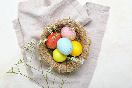Nest with beautiful Easter eggs and flowers on light background