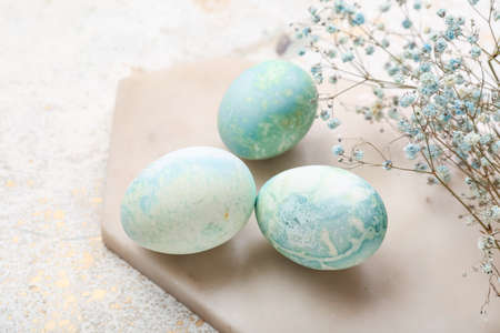 Board with beautiful Easter eggs and gypsophila flowers on light background, closeup