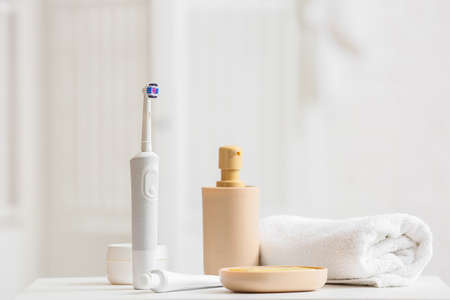 Electric toothbrush, cosmetic products and rolled towel on tableの写真素材