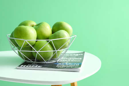 Basket with apples and magazine on table near color wallの写真素材