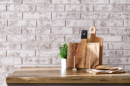 Wooden cutting board and bread on table near brick wall