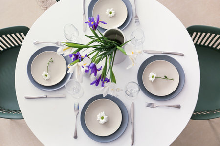 Dining table with stylish setting and vase with iris flowers served for International Women's Day...
