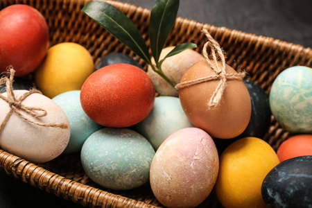 Wicker basket with multicolored Easter eggs on dark background