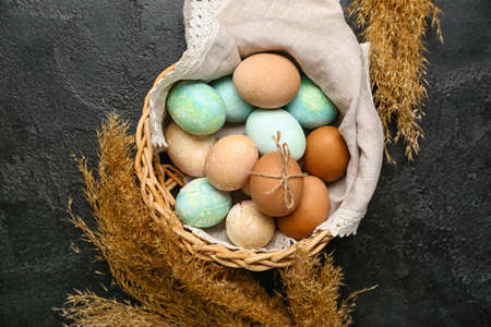 Wicker basket with painted Easter eggs, napkin and spikelets on dark background