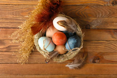 Nest with multicolored Easter eggs, feathers and spikelets on wooden background