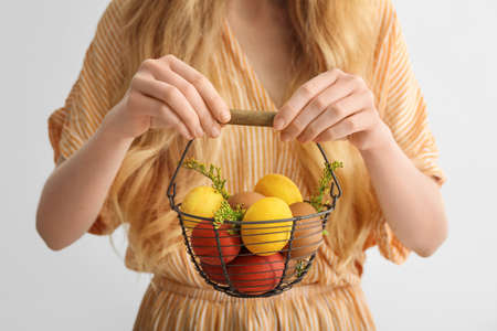 Woman holding basket with painted Easter eggs on light backgroundの写真素材
