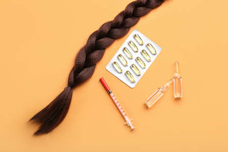 Braided hair strand with pills, syringe and ampules on orange background