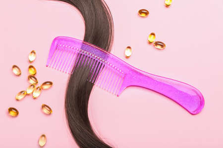 Brunette hair strand with comb and pills on pink backgroundの写真素材