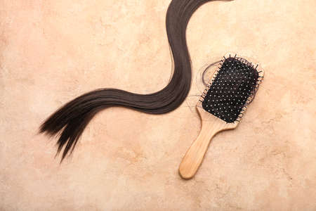 Brush with clump and brunette hair strand on beige background